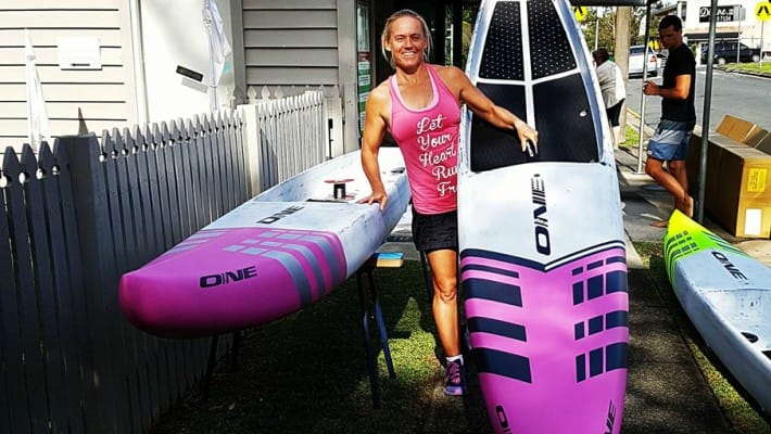 Angela Jackson poses in front if two boards from her very own brand ONE Stand Up Paddle